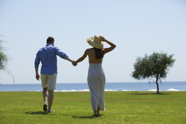 Couple holding hands walking on the lawn and towards the beach at Apollo Blue Hotel